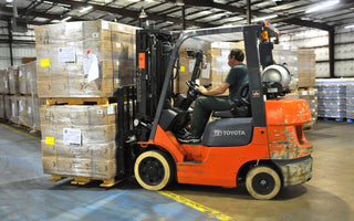 Operator driving a forklift with palletized cartons inside a warehouse — FEMA public-domain photo, illustrative