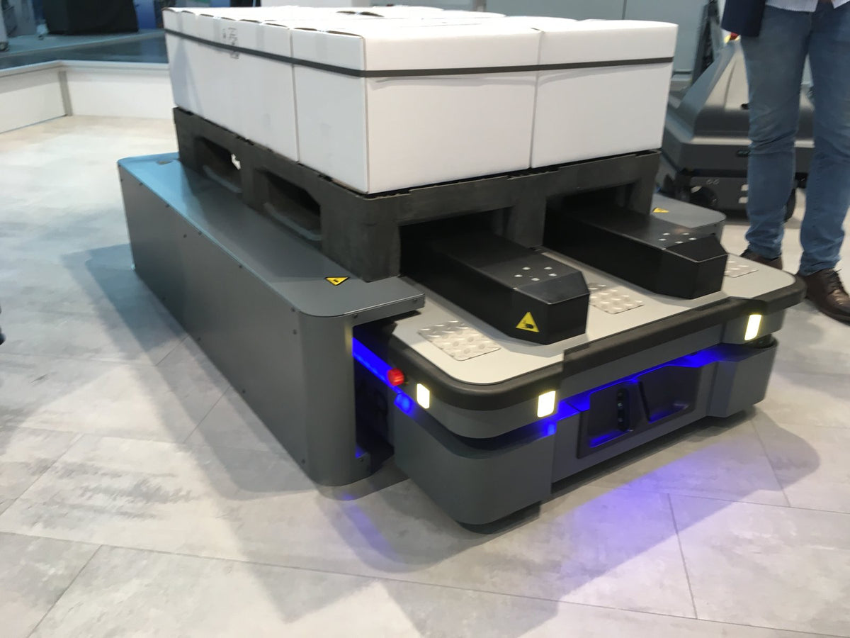 Low-profile warehouse autonomous mobile robot carrying a pallet of boxes — illustrative AMR stand-in, not an FCC photo