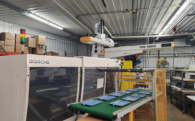 Injection molding machine with robot arm and conveyor trays, illustrative manufacturing cell, not the Tiffin Kreate plant