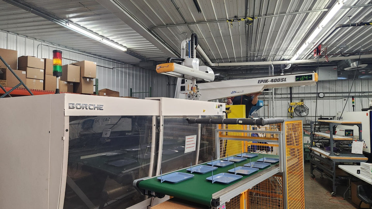 Injection molding machine with robot arm and conveyor trays, illustrative manufacturing cell, not the Tiffin Kreate plant